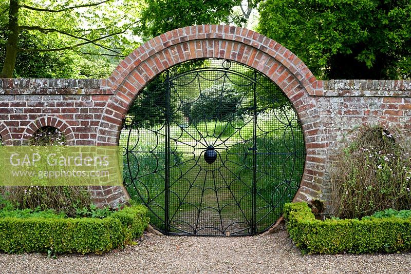 Spider Gate, looking from walled garden to woodland. Gravel pathway with clipped Buxus sempervirens edging and Felicia petiolata in arches