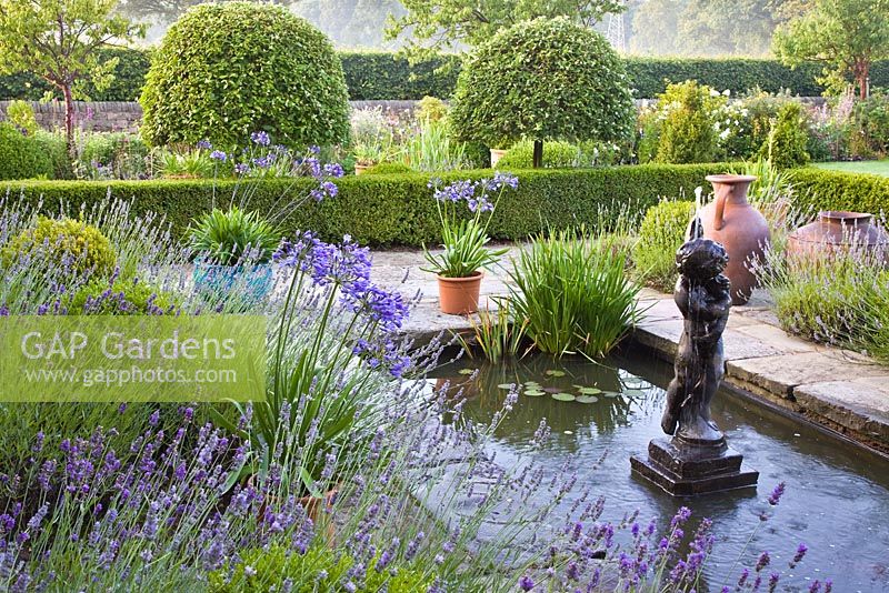 Semi formal garden Blue Boy statue formal pond paved margins containers with Agapanthus Wilkins and borders of Lavender Pleck, NGS, Whitmore near Newcastle-under-Lyme in North Staffordshire