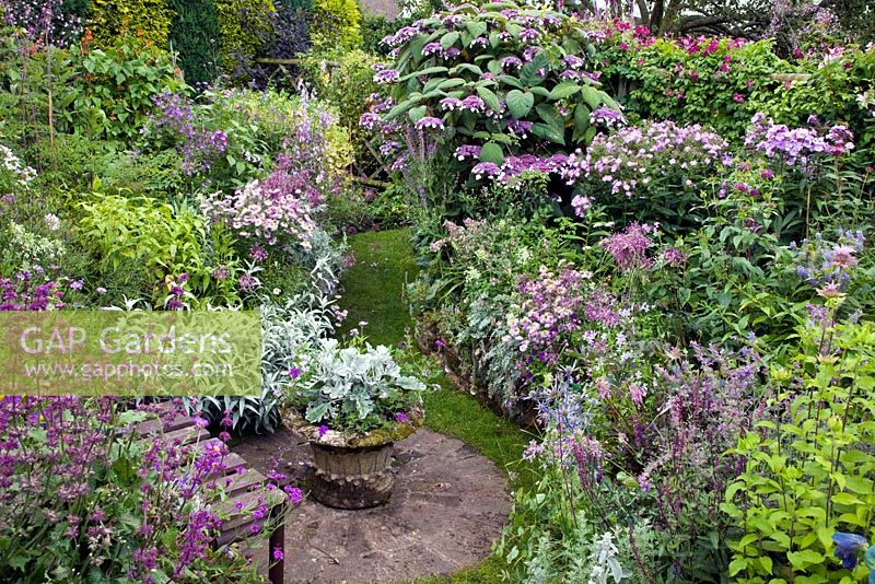 Colour themed borders of herbaceous perennials brick circle with well planted container wooden seat in The Dell with flowers in profusion, packed into an idyllic English cottage garden, at Grafton Cottage , NGS 