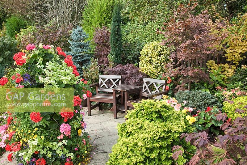 Seating area with mature shrubs and trees, well planted summer basket on stand, crazy paving path in late Summer early Autumn at Four Seasons (NGS) Walsall Staffordshire