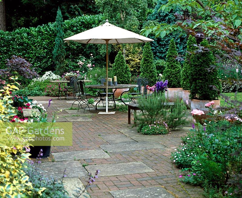 Outdoor seating area with white parasol screened with conifer pots - West Dean