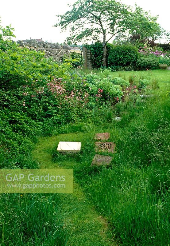 Country garden, path mown through long grass. A small dip at the bottom of the garden provides a sheltered opportunity for seating. Naturalistic border, dry stone wall.