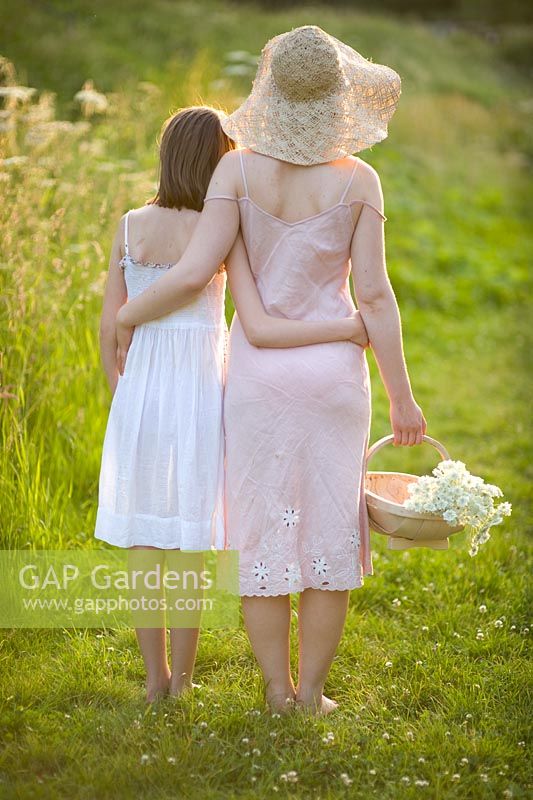 Woman and girl walking in evening summer sunlight, carrying a trug of picked flowers