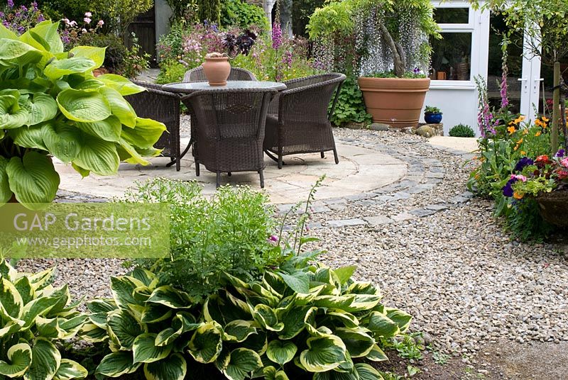 Rattan chairs and table on circular stone and gravel patio - Montford Cottage, NGS garden, Lancashire