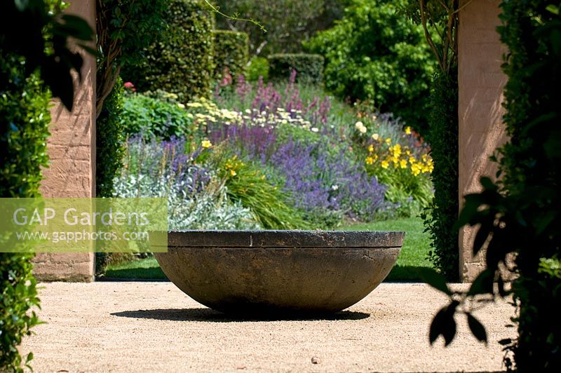 Courtyard gravel garden surrounded by pergola with central stone pond bowl and view thorugh to herbaceous border - The Garden Vineyard, Victoria, Australia
