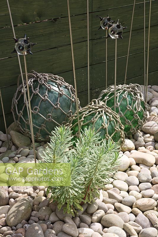 Seaside Inspired garden. Euphorbia 'Silver Swan' growing in pebbles with glass fishing floats and glass topped decorations.