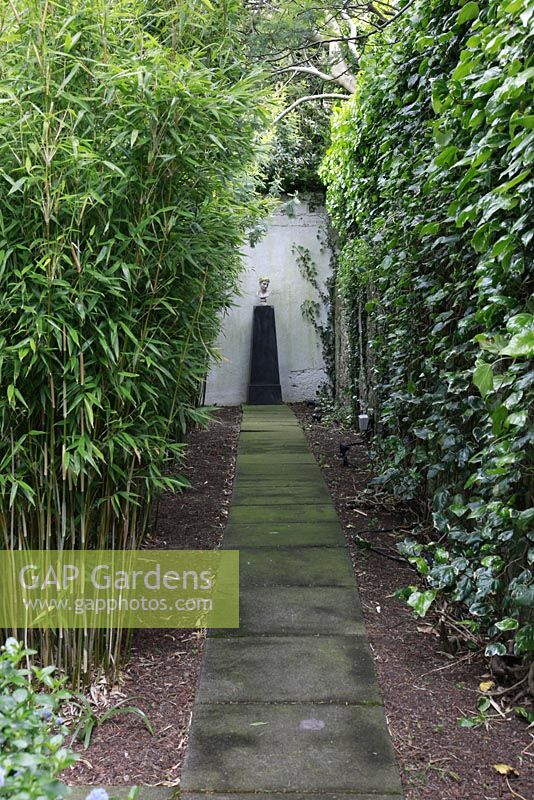 Path with focal point in suburban family garden for restored Art Deco house. Tall hedge and Bamboo
