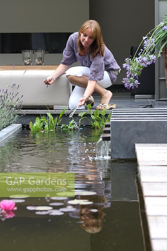 Urban garden in summer with terrace and pond. Woman feeding fish. Agapanthus.