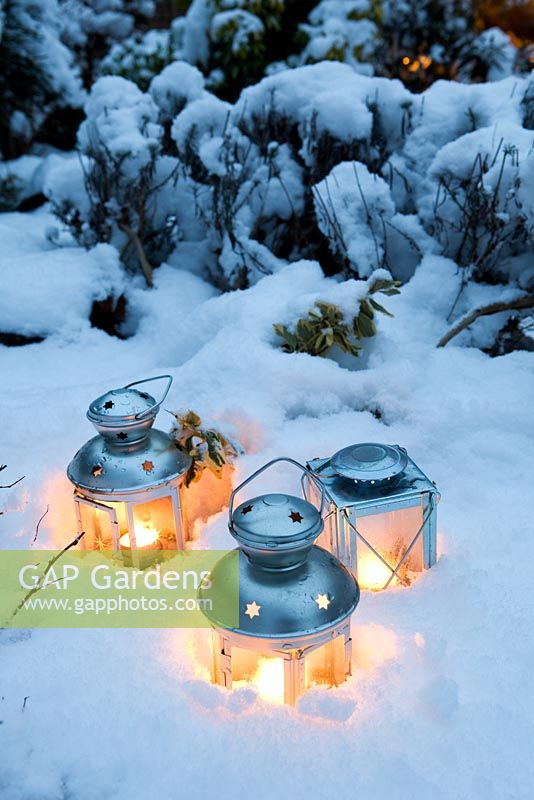 Three tea light candle lanterns set in snow on flower bed
