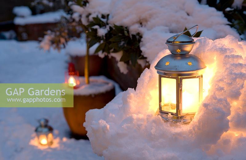 Tea light candle lanterns set in miniature snow grotto and around container grown plants