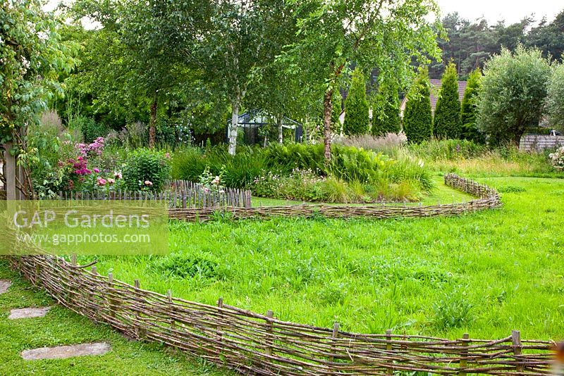 Meadow area in garden with woven willow fencing. 