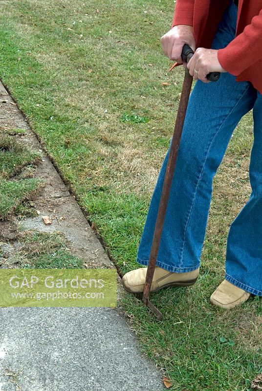 Woman tidying the edge of grassed area alongside path using edging iron