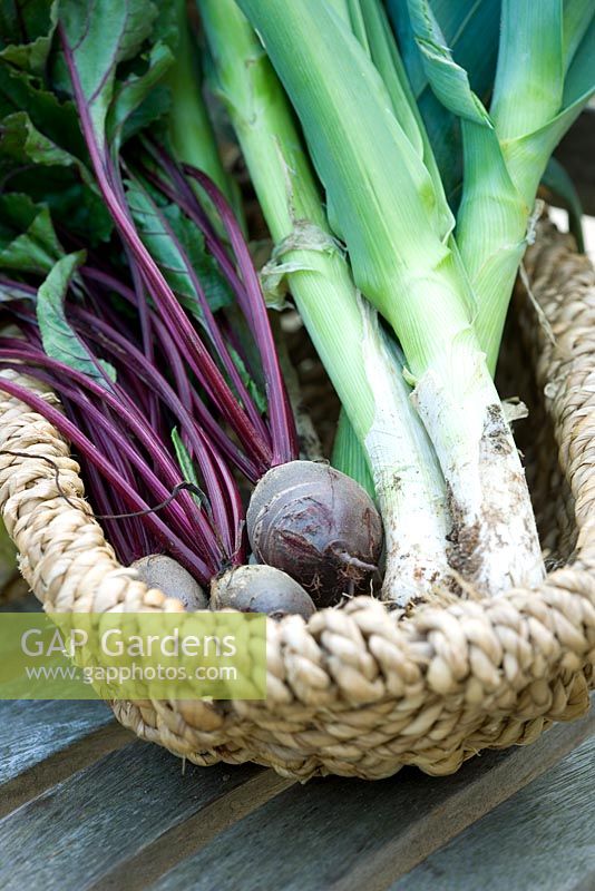 Leeks 'Pancho' and beetroot 'Bolthardy' in a wicker basket on a wooden table