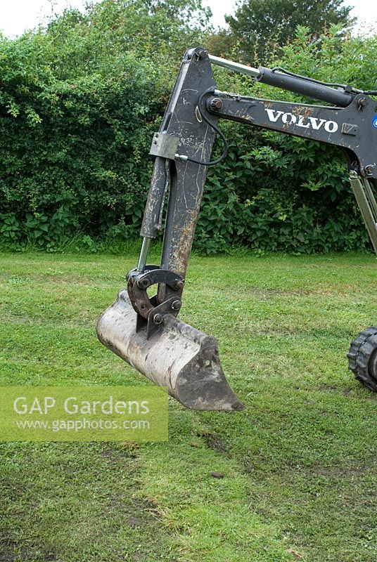 Mouth of a digger being used to flatten newly laid turf