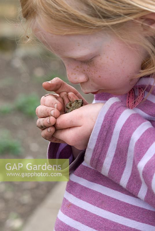 Young girl holding a common frog and blowing it a kiss