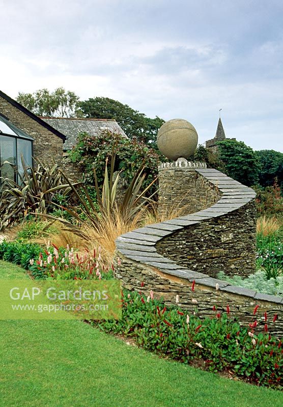 'Question mark' wall and millenium Globe designed and built by owner John Bracey. Planted at base with Persicaria affinis 'Superba'.  Scypen, Ringmore, Devon