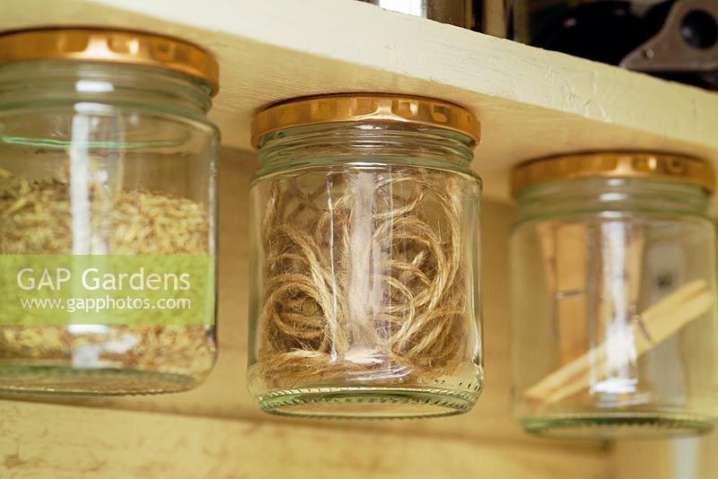 Glass jars with pegs and twine - jar lids are stuck to top of shelf