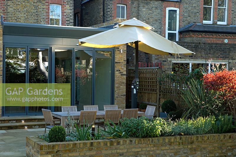 Contemporary urban garden with lighting, seating area with parasol on terrace and raised brick bed border - London
