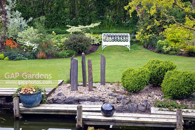 Pond area, decking with silver balls, tall grey slate plinths, mature shrubs and trees - John Massey's Garden NGS, Ashwood, West Midlands
