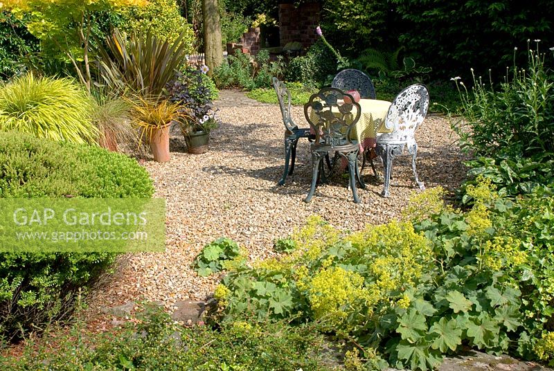 Decorative metal table and chairs in summer gravel garden at 'Hazelwood', Jacqueline Iddon Hardy Plants, NGS garden, Lancashire 