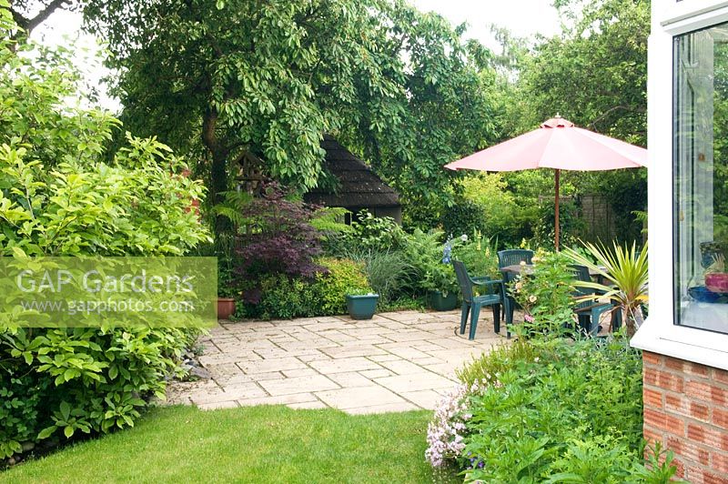Patio in cottage garden with parasol over seating area. Windy Corner NGS, Barton, Cambs, UK
