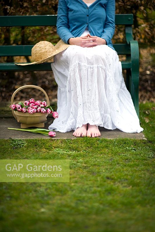 Woman seated on a garden bench with a sunhat and a trug of tulips