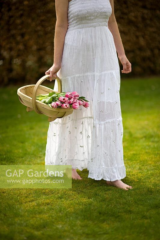 Woman wearing a white dress carrying a trug of Tulips