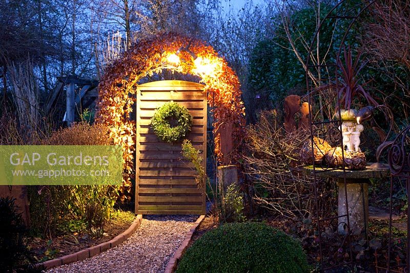 Garden in winter with wreath and lights over archway