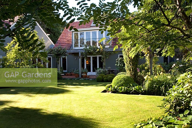 Country garden with neat lawn. House painted grey with terracotta roof tiles. Christchurch, New Zealand