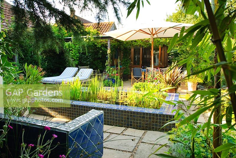 Paved courtyard with loungers and raised pool clad in blue glazed tiles.