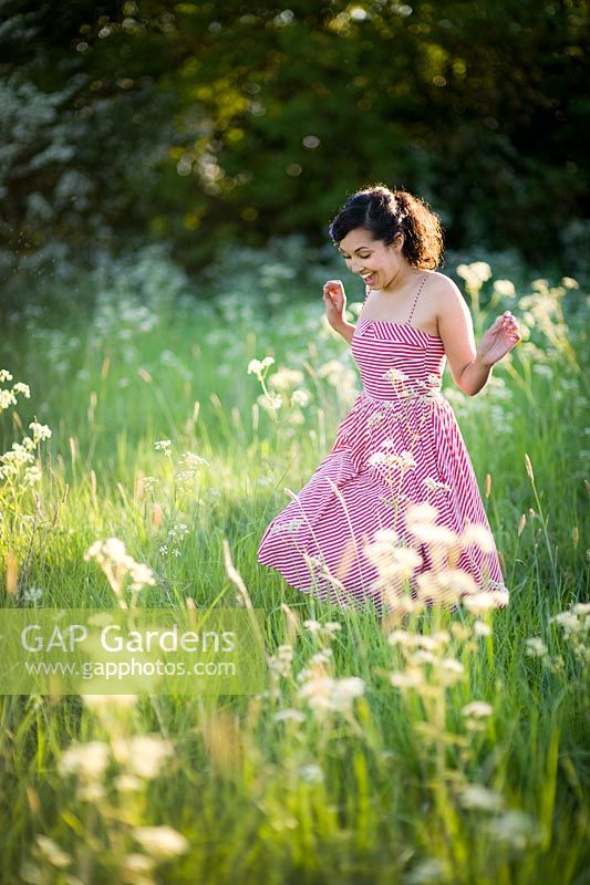 Woman in a red dress running through a meadow in evening sunlight