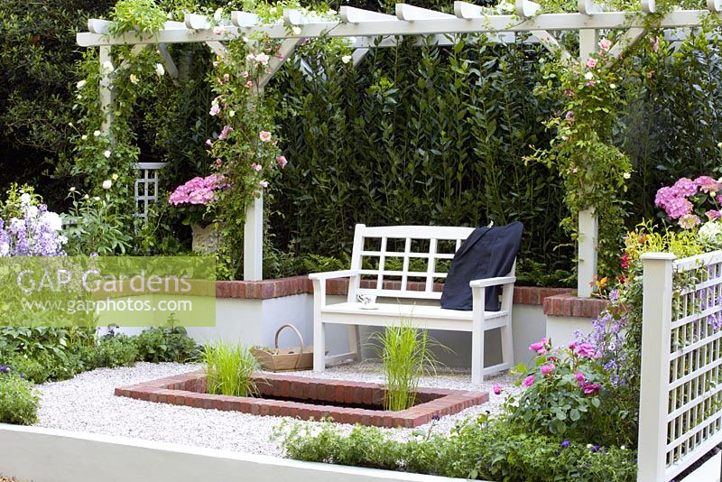 Small gravelled courtyard with wooden seat under pergola, pool and colourful borders. The 'Christian before Dior' garden - Bronze medal winner at RHS Chelsea Flower Show 2010
 
