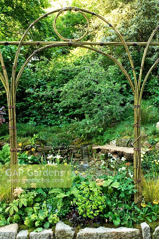 Natural arch above border of Iris Trollius, Rodgersia and Alchemilla mollis, Corylus maxima 'Purpurea', Primula chungensis. Small waterfall. The 'Music on the Moors' garden - Gold medal winner at RHS Chelsea Flower Show 2010 