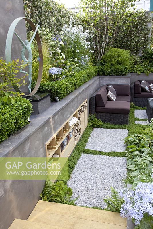 Sunken patio area with storage built into wall of raised bed and wicker furniture. 'A Joy Forever' Garden, Silver medal winner at RHS Chelsea Flower Show 2010 