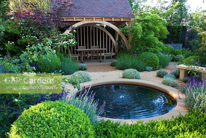 A circular pool with seating and a green oak summerhouse with planting of Buxus, Lavandula, Roses and Viburnum in The M&G Garden, Gold medal winner, RHS Chelsea Flower Show 2010 