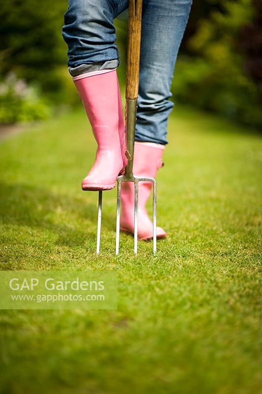 Woman wearing pink wellies and jeans, using a garden fork