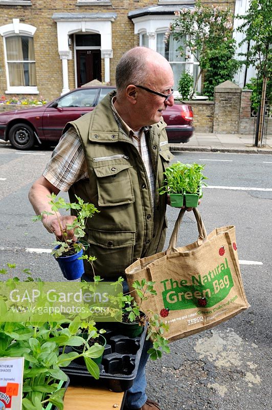 Man carrying a reusable bag, buying plants from a stall in an urban street, Hackney, London