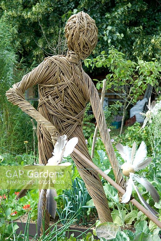 Scarecrow created from willow, representing a working gardener, with potato and feather bird-scarers on string across vegetable bed.  'Shakespeare Allotment' - Bronze Medal Winner - RHS Hampton Court Flower Show 2010