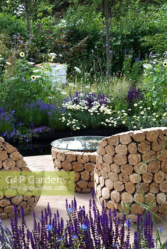 Log table and chairs surrounded by bee friendly plants such as Verbena bonariensis, Helianthus annuus 'Italian White', Salvia, Ammi majus and Leucanthemum - 'The Copella Bee Garden', Silver Gilt medal winner at RHS Hampton Court Flower Show 2010