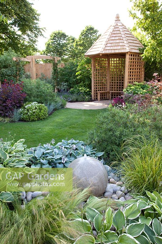Stone water feature, plantings of Hosta and Stipa tenuissima with gazebo in background - The Urban Retreat, Bronze medal winner at RHS Hampton Court Flower Show 2010