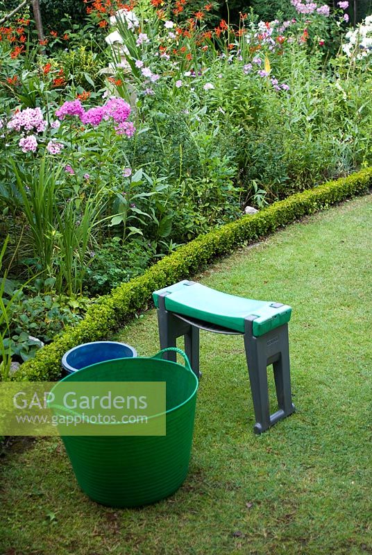 Tubtrug - plastic garden tub with handles - and kneeler on lawn with summer herbaceous border edged by clipped Buxus
