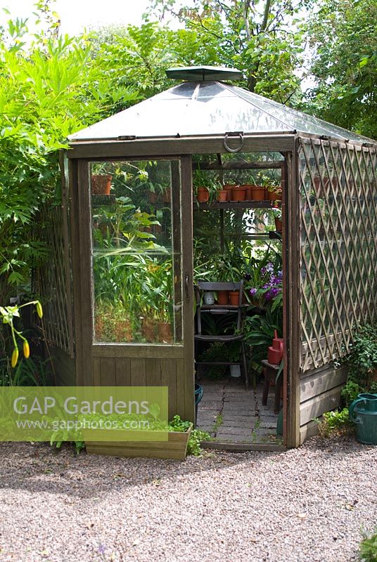Hexagonal wooden greenhouse full of tender plants at Crossing House Garden, Cambridgeshire
