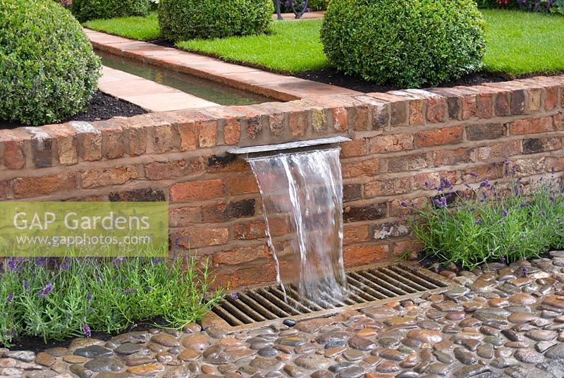 Water flowing along a rill, edged with conical Buxus - Box topiary, and falling over brick wall into drain and cobbled surface. The Russell Watkinson Landscapes 'It's a Reflection of Life' garden - RHS Tatton Flower Show 2010