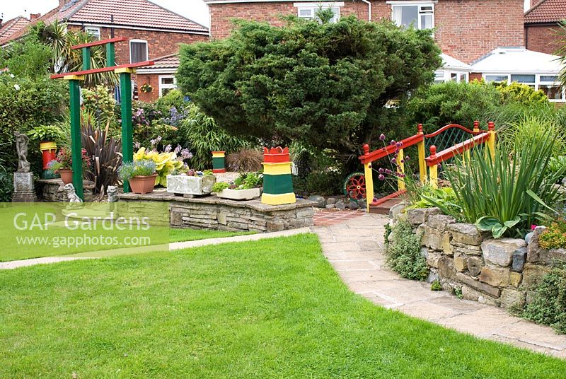 Back garden with interesting reclaimed garden items including statues, chimney pots, stone troughs, and a painted Japanese style bridge. Meadow Ave, Southport, Lancashire. The garden opens for The National Gardens Scheme