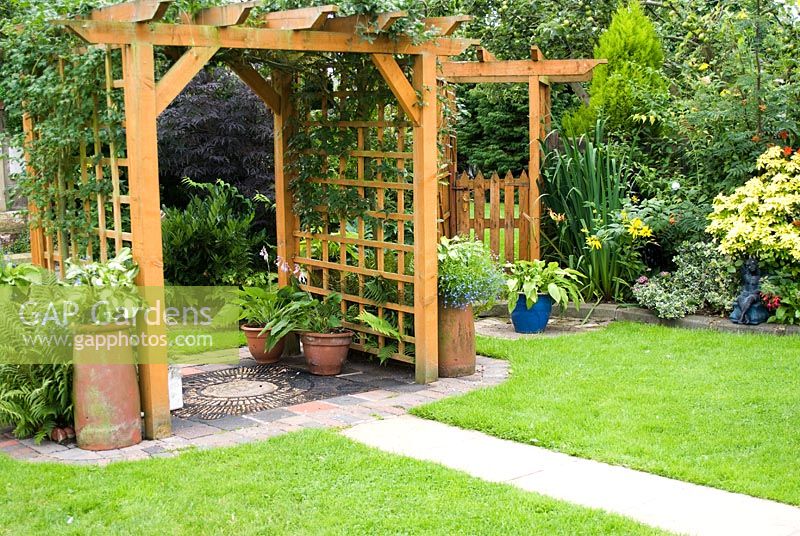 Wooden pergola with decorative path and climbers. Pots containing Ferns and Hosta and smaller arbour with gate. Meadow Ave, Southport, Lancashire. The garden opens for The National Gardens Scheme