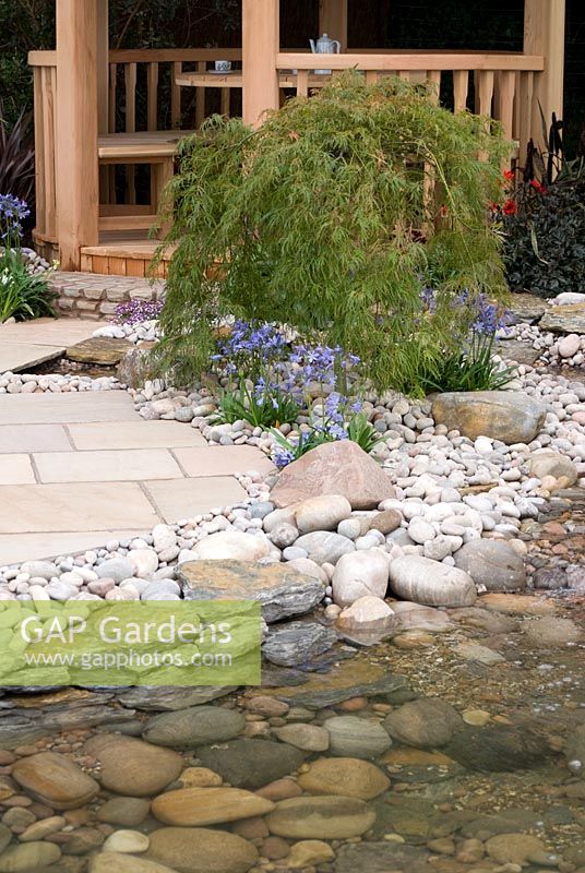 Pebble and cobble edged stream flowing past wooden circular summerhouse. The Pond Company 'Water way to go' garden.  RHS Tatton Flower Show 2010 