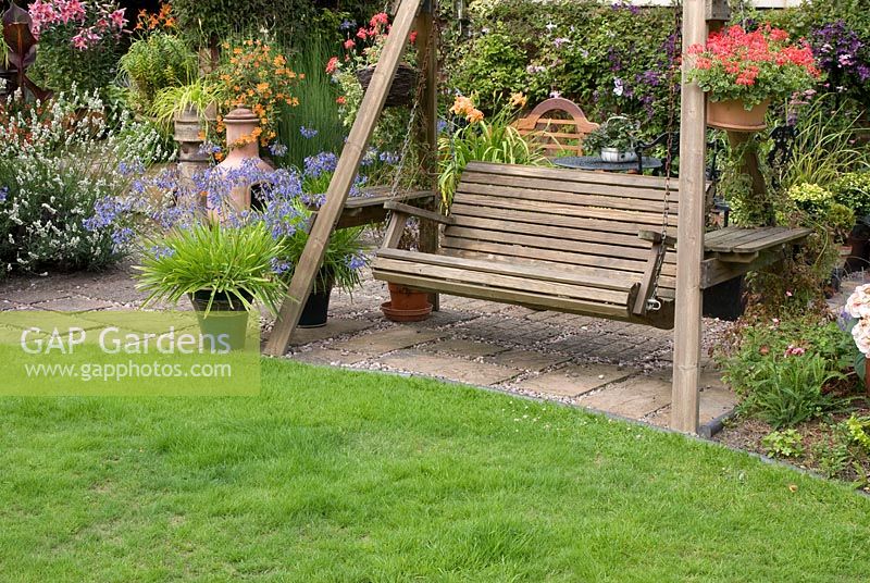 Swing wooden bench on patio with colourful containers.  Saxon Road, Lancashire. The garden is open for The National Garden Scheme