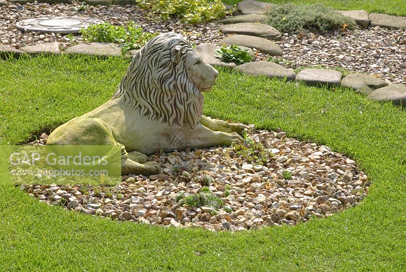 Stone lion statue in circular bed with gravel by lawn, with gravel and stone path beyond at 'Trevinia', Stubbins, Lancashire NGS