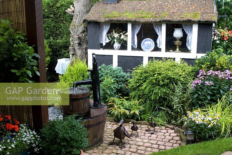 Decorative painted garden shed with thatched roof, border with Phlox, Lonicera nitida and conifers, oak barrel water feature with metal duck sculptures - Trevinia', Stubbins, Lancashire, NGS