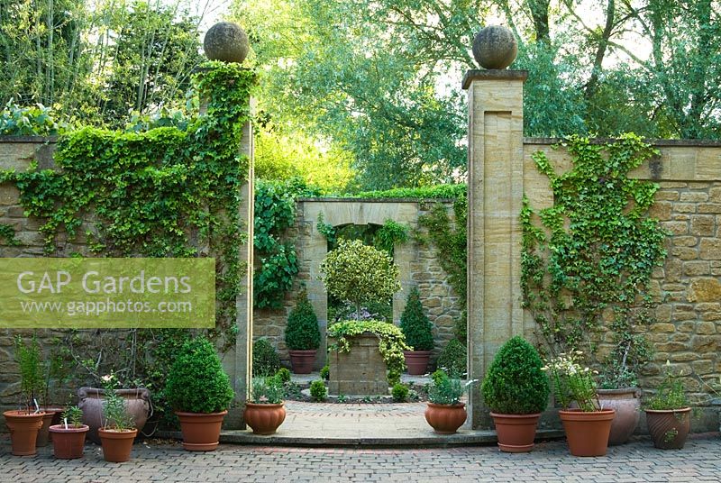 Entrance to a small formal 'antechamber' to walled garden, built 1999, designed by late Graham Hopewell, planted with a combination of cool evergreens including low hedges of Hedera 'Ivalace', clipped box and standard holly - Mill House, Netherbury, Dorset